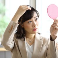 鏡で頭を見る女性